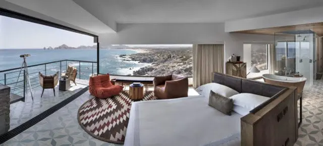 Bedroom with king-size bed, freestanding copper tub, glass-enclosed shower, and balcony overlooking the ocean.