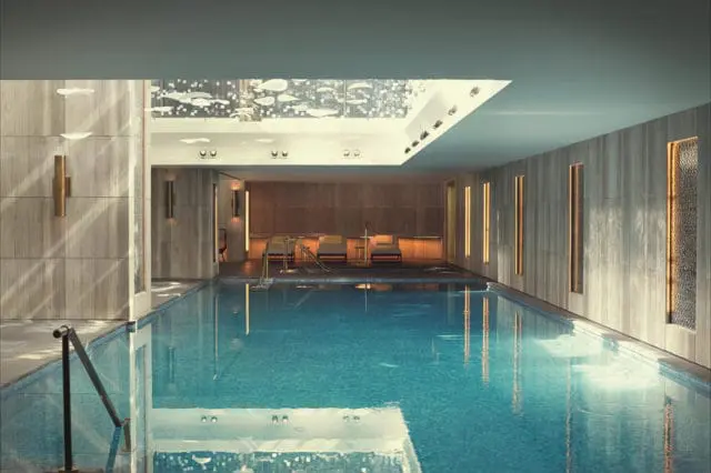 Indoor swimming pool with bright blue water, wood-paneled walls, and recessed lighting. Lounge chairs are visible at the far end.