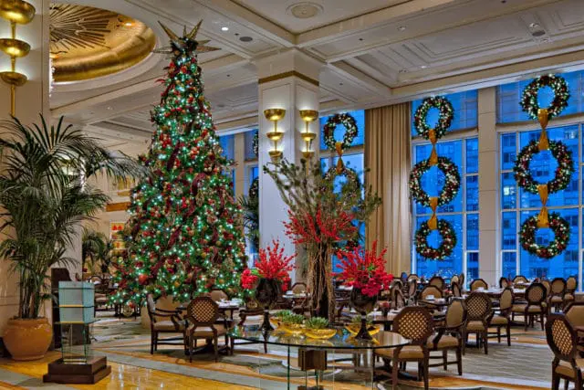 Elegant hotel lobby decorated for Christmas with a large, illuminated tree, festive wreaths on windows, and floral arrangements.