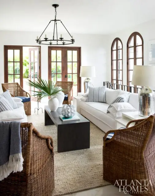 Living room with white sofa, wicker chairs, dark wood coffee table, and arched windows. A black chandelier hangs overhead.