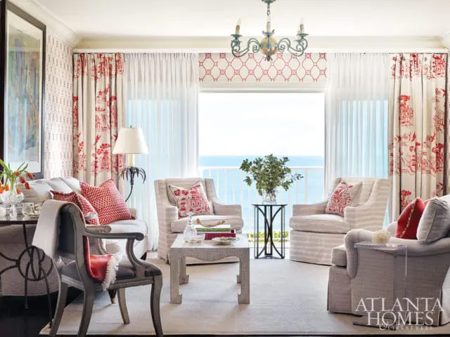 Living room with a view of the ocean, featuring striped armchairs, red and white patterned curtains, and a chinoiserie wallpaper accent.
