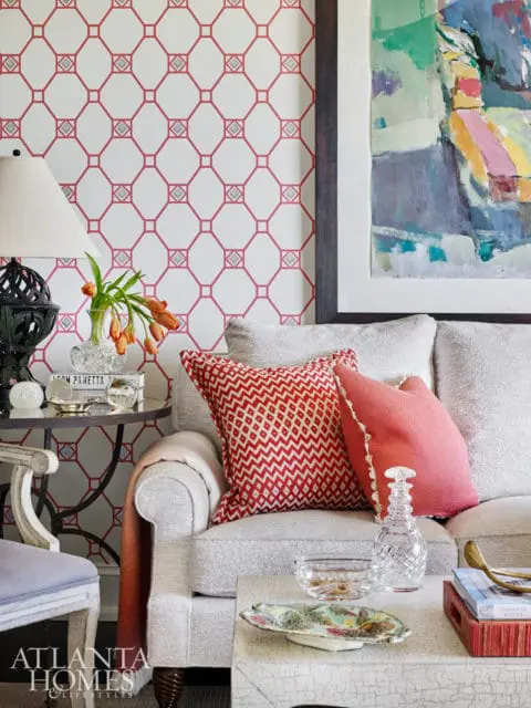 Living room with white and red geometric wallpaper, a light gray sofa with red patterned pillows, and a colorful abstract painting.