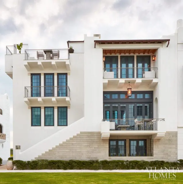 Modern white stucco house with multiple balconies, dark-framed windows, and a wide staircase leading to the entrance.