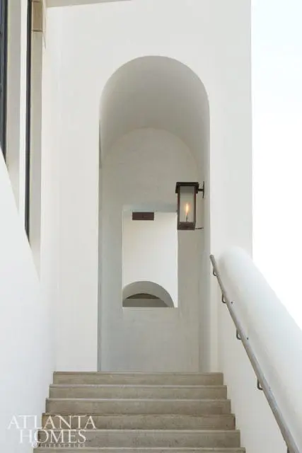 Concrete stairs leading up to an arched entryway with a lantern and a reflection of another archway