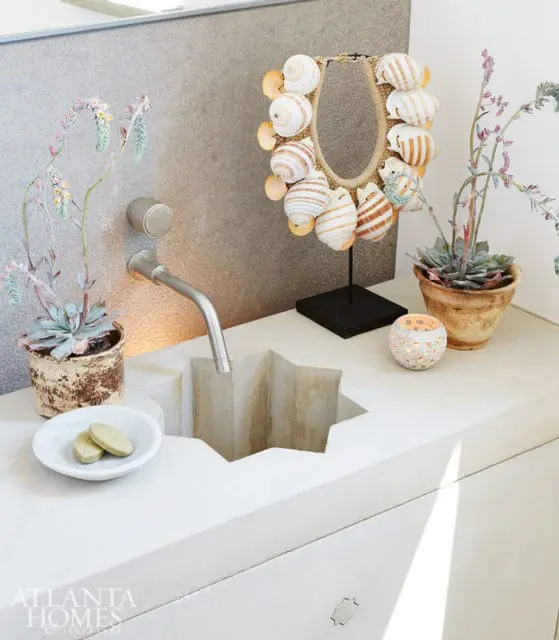 White concrete vanity with a star-shaped sink, brushed nickel faucet, and decorative shell necklace display. Succulent plants and a small candle add decorative touches.