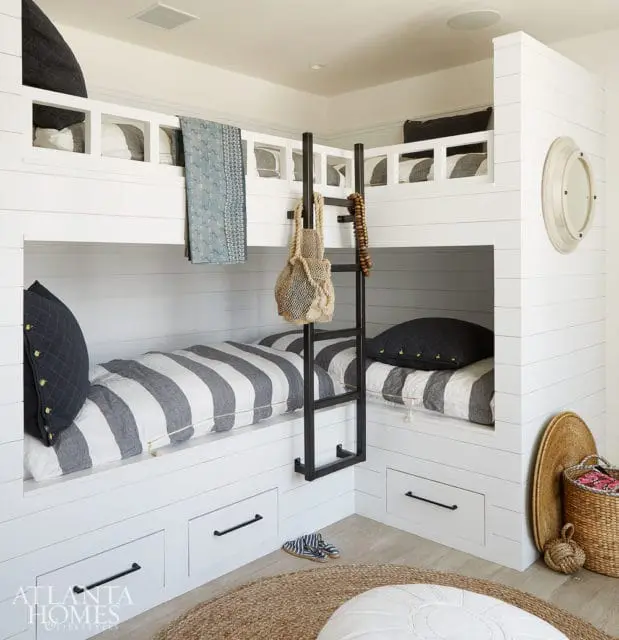 White shiplap bunk beds with gray and white striped bedding, dark gray quilted pillows, and a black ladder. A woven bag hangs from the ladder.