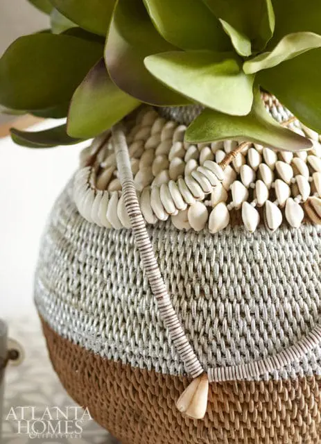 Woven basket with white shells and beads, topped with green succulent leaves. Atlanta Homes & Lifestyles logo in bottom left corner.