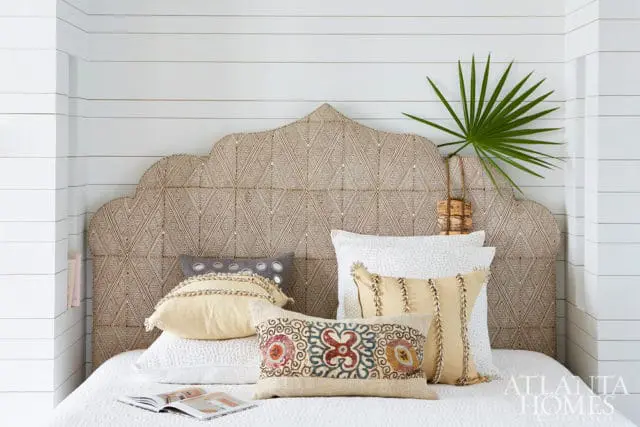 Bedroom with a scalloped headboard upholstered in a diamond pattern fabric, white shiplap walls, and a bed with white and yellow patterned pillows.