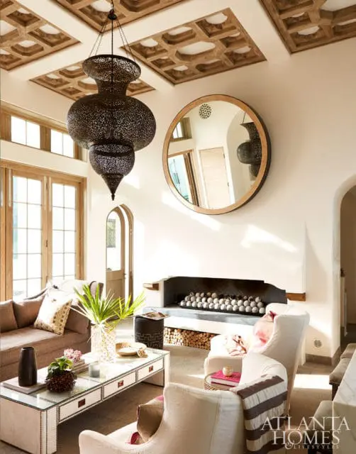Living room with coffered wood ceiling, ornate metal pendant light, round mirror, and fireplace with decorative balls.