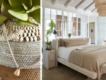 Bedroom with a neutral palette, featuring a king-size bed with beige linens, a decorative pillow, and a woven basket with shells and greenery in the foreground.