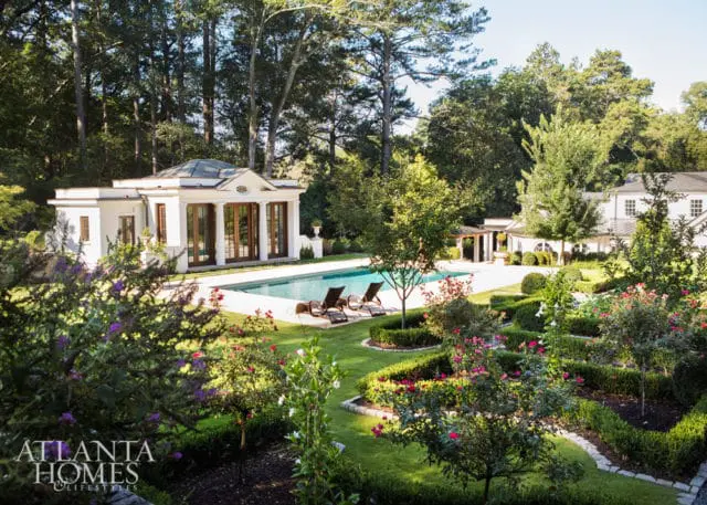 Estate grounds with a rectangular swimming pool, pool house with columns, and manicured gardens featuring rose bushes and boxwood hedges.