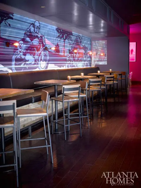 Bar area with dark wood floors, leather banquette seating, and tables with metal-frame stools. A large mural of motorcyclists and palm trees covers the back wall.