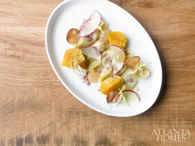 White oval plate with a dish of ravioli topped with roasted squash, thinly sliced radishes, and a creamy sauce, set on a wooden table.