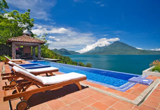 Infinity pool overlooking a large lake with mountains in the background under a blue sky with white clouds.