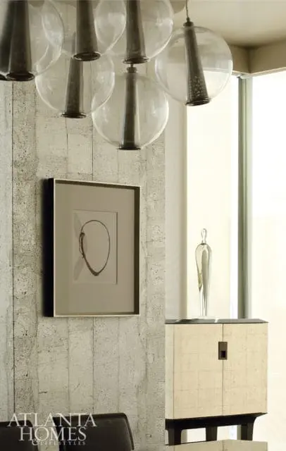 Modern dining room with textured gray walls, a large abstract artwork, a glass globe chandelier, and a cream-colored cabinet with a dark square pull.