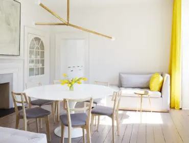 Dining room with white oval table, gray upholstered chairs, fireplace with marble surround, built-in cabinet, and yellow curtains.