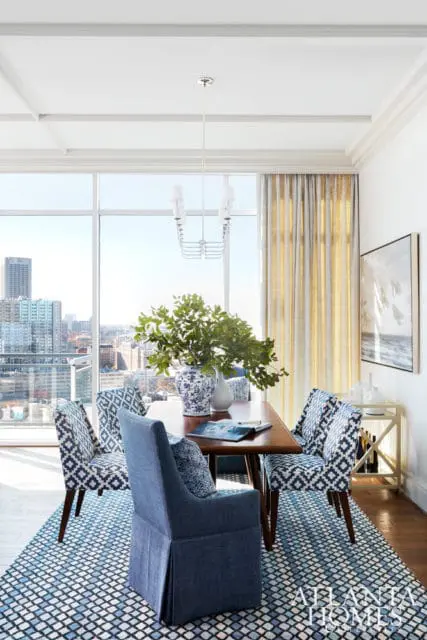 Dining room with a wooden table, blue patterned chairs, and a large window overlooking a city skyline.