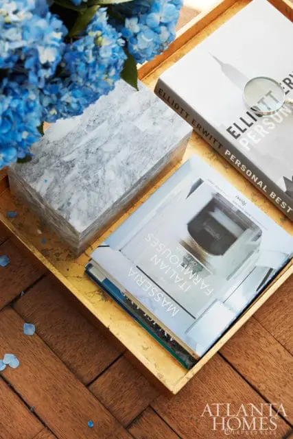 Gold tray with a marble box, two books titled 'The Masseria: Italian Farmhouses of Puglia' and 'Elliott Erwitt Personal Best', a magnifying glass, and blue hydrangeas.