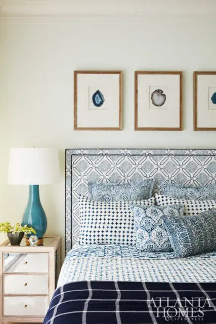 Bedroom with a blue and white patterned headboard, matching pillows, and a mirrored nightstand with a turquoise lamp. Three framed agate slices hang on the wall above the bed.