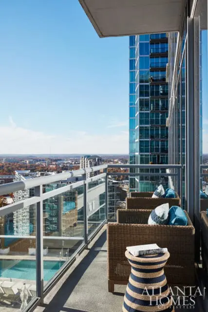 Balcony with wicker chairs and blue cushions overlooking a city skyline and pool.
