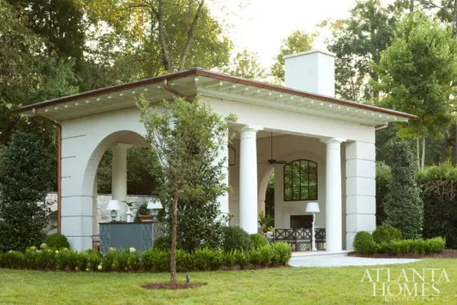 White brick pavilion with arched openings, Doric columns, and a copper gutter system, surrounded by manicured greenery and mature trees.