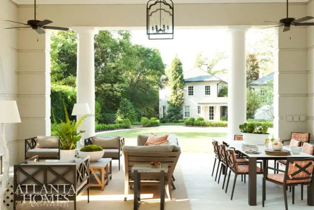 Covered porch with seating area and dining table, overlooking a manicured lawn and white house.