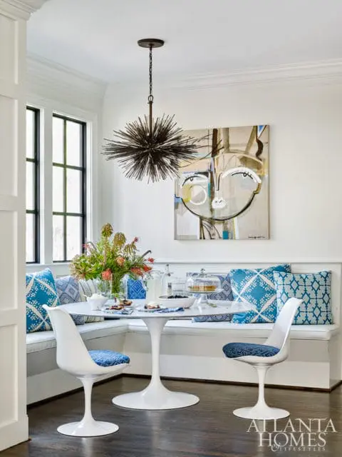 Breakfast nook with white banquette seating, blue patterned pillows, tulip table, and abstract face art.
