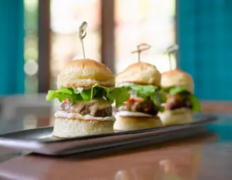 Three gourmet sliders on a rectangular silver platter, garnished with toothpicks and lettuce.