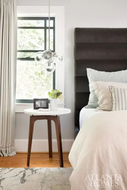 Bedroom with a dark upholstered headboard, light-colored bedding, and a marble-top side table with a glass pendant light above.