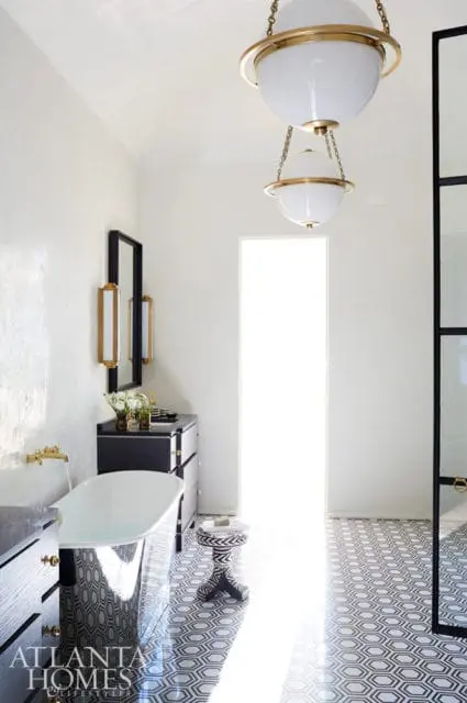 Modern bathroom with freestanding tub, black vanity, geometric floor tile, and globe pendant lights with brass accents.