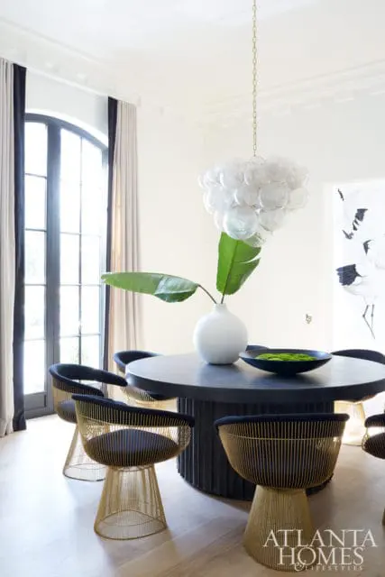 Dining room with a round dark wood table, black chairs with gold wire bases, and a clear bubble chandelier.