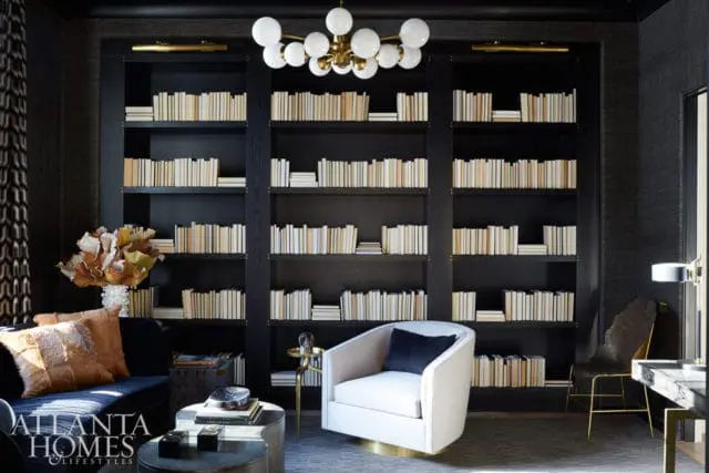 Dark wood built-in bookshelves filled with light-spined books, a white swivel chair with a navy cushion, and a dark blue sofa with fur pillows.