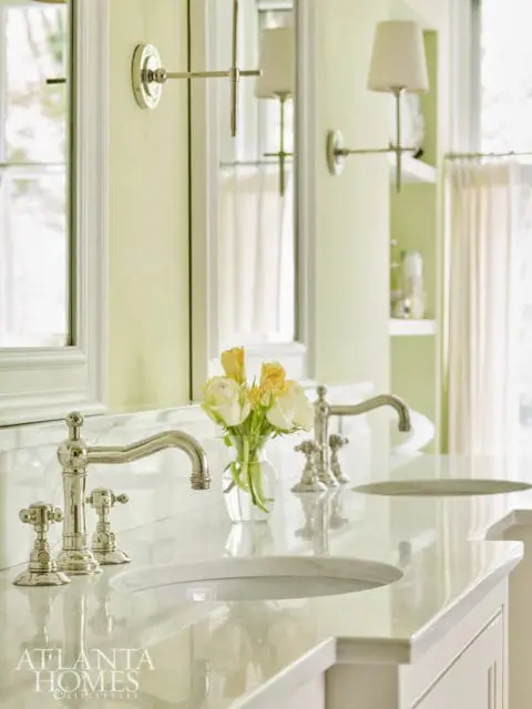 Double vanity bathroom with white marble countertop, polished nickel faucets, and a vase of yellow and white roses. Pale green walls and white trim are visible.