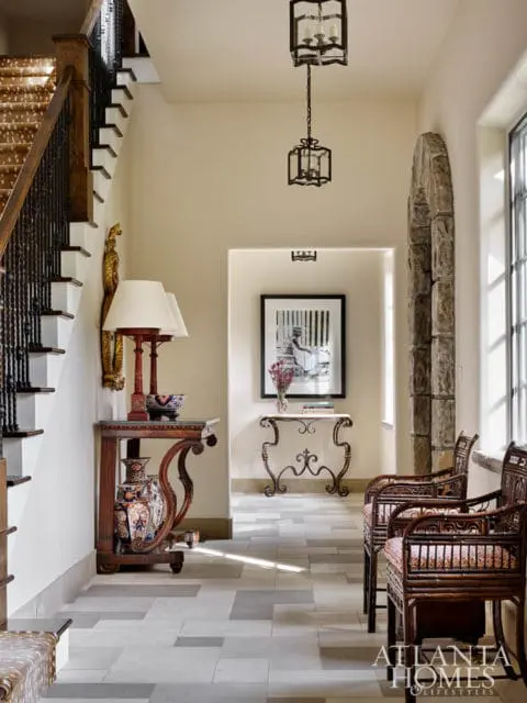Hallway with a staircase, two hanging lanterns, stone archway, and two bamboo chairs with patterned cushions.