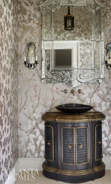 Powder room with botanical wallpaper, ornate mirrored vanity, and dark wood cabinet with brass accents.