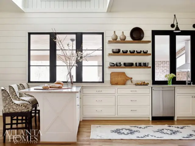 White shiplap kitchen with marble island, stainless steel appliances, open shelving, and black framed windows.