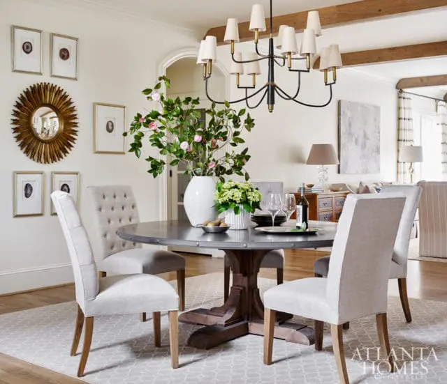 Round metal dining table with tufted upholstered chairs in a room with a sunburst mirror, framed agate prints, and a multi-light chandelier.