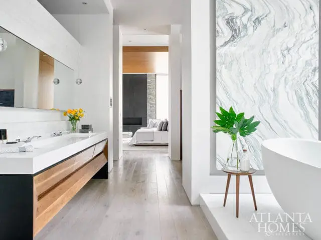 Modern bathroom with double vanity, wood cabinetry, and a freestanding tub. A large marble slab adorns the wall next to the tub.
