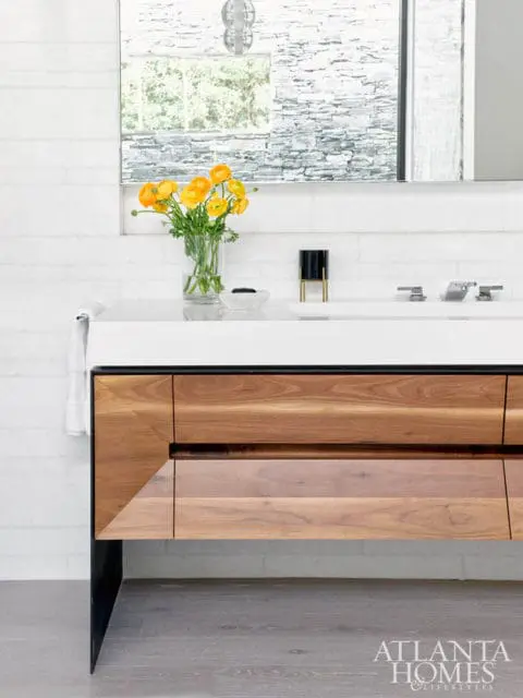 Modern bathroom vanity with warm wood drawers and black metal legs, white quartz countertop, and a vase of yellow flowers.