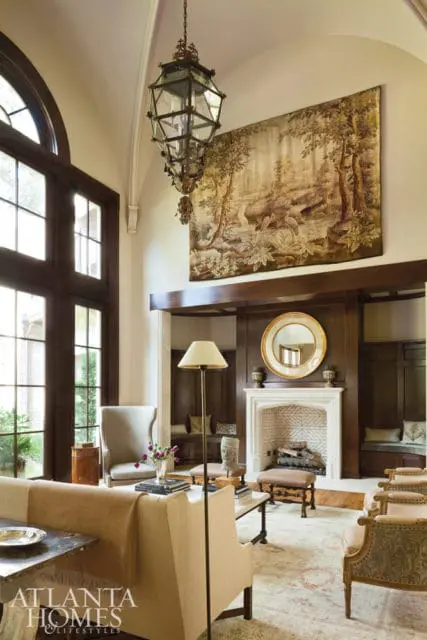 Living room with a large tapestry above a fireplace, a tall arched window, and upholstered furniture.