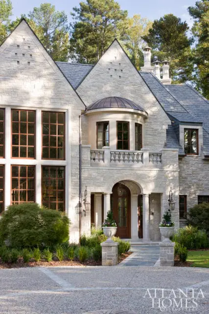 Stone mansion with multiple gabled roofs, large grid windows, a rounded balcony, and an arched wooden entryway.