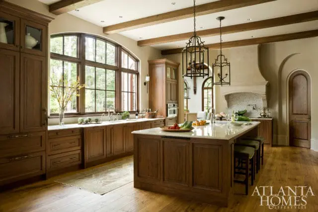 Warm wood kitchen with marble island, arched window, and wrought iron chandeliers.