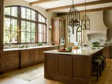 Warm wood kitchen with a large arched window, marble island with seating, and ornate hanging lanterns.