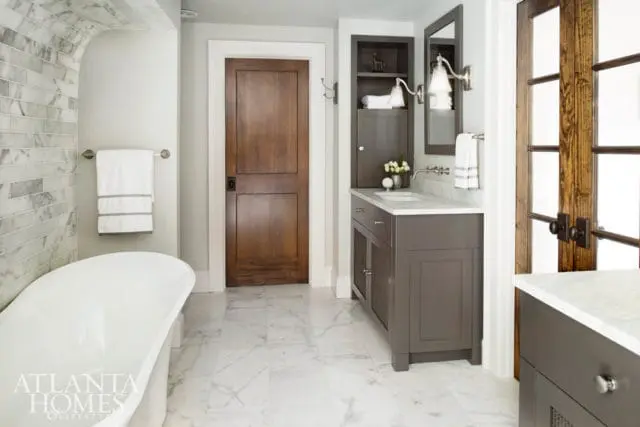 Bathroom with white freestanding tub, marble tile accent wall, dark wood door, and gray vanity with marble countertop.