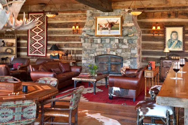 Log cabin living room with leather sofas, stone fireplace, antler chandelier, and Native American-inspired textiles.