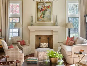 Living room with a cream-colored sofa, plaid armchairs, a stone fireplace with a floral painting above, and a grandfather clock.