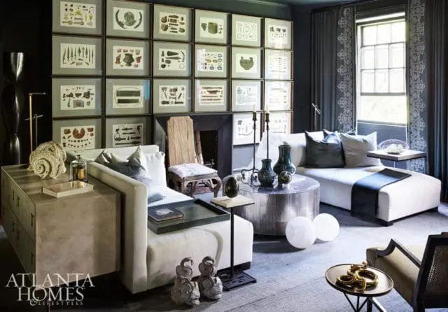 Living room with a wall of framed botanical prints, a sectional sofa, a round metal coffee table, and dark blue curtains.