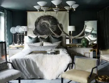 Dark green bedroom with a large ammonite fossil art above the bed, plush white rug, cane chairs, and ornate lamps.