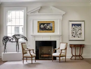 Living room with white fireplace, two upholstered armchairs, a metal horse sculpture, and artwork on the walls.