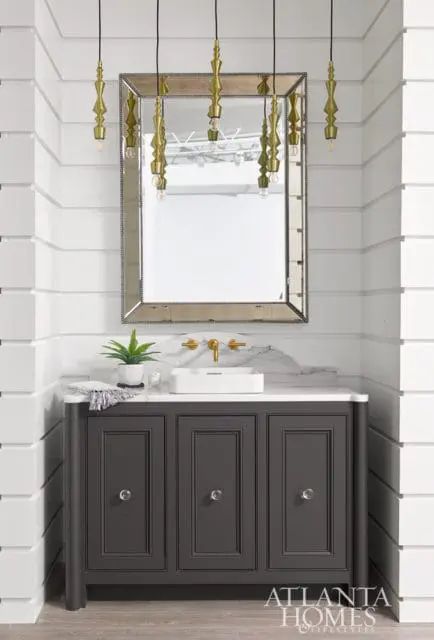 Dark gray vanity with white rectangular sink, marble backsplash, and ornate gold pendant lights hanging above a mirrored frame